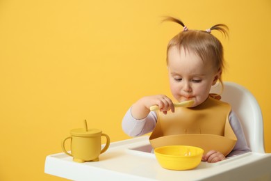 Cute little baby wearing bib while eating on yellow background