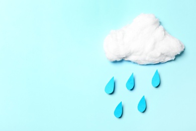 White cotton cloud and paper drops imitating rain on cyan background, flat lay. Space for text