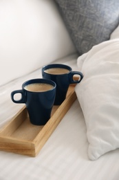 Wooden tray with cups of coffee near soft blanket on bed