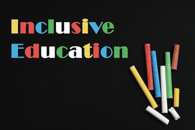 Phrase INCLUSIVE EDUCATION and colorful chalks on blackboard, flat lay