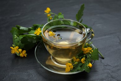 Glass cup of aromatic celandine tea and flowers on black table
