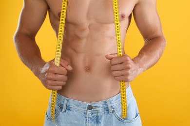 Shirtless man with slim body and measuring tape on yellow background, closeup