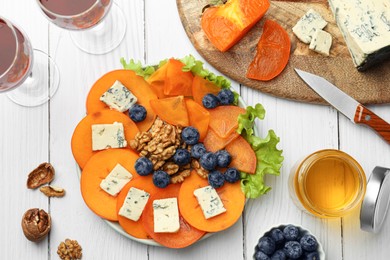 Photo of Delicious persimmon with blue cheese on white wooden table, flat lay