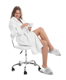 Young woman in bathrobe with cup of beverage on white background
