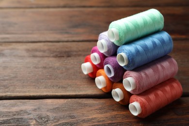 Photo of Stack of colorful sewing threads on wooden table. Space for text