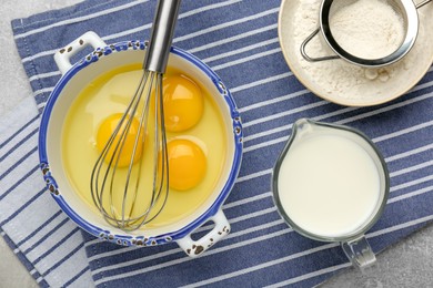 Whisk, eggs, milk and flour on grey table, flat lay