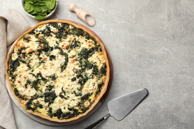 Photo of Delicious homemade quiche, fresh spinach leaves and spatula on light gray table, flat lay. Space for text