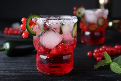 Photo of Spicy red currant cocktail with jalapeno on black wooden table