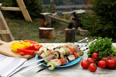 Metal skewers with raw marinated meat and vegetables on wooden table outdoors