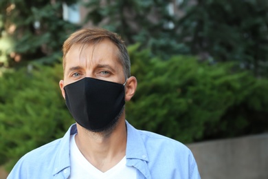 Man wearing handmade cloth mask outdoors, space for text. Personal protective equipment during COVID-19 pandemic
