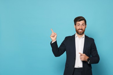 Photo of Smiling bearded man pointing index finger up on light blue background. Space for text