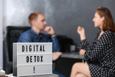 Colleagues chatting in office, focus on lightbox with phrase DIGITAL DETOX