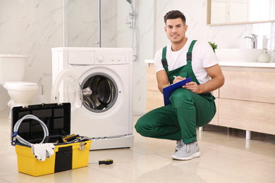 Repairman with clipboard and toolbox near washing machine in bathroom