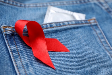 Jeans with red ribbon and condom, closeup. AIDS disease awareness