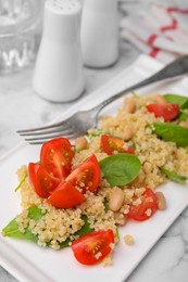 Photo of Delicious quinoa salad with tomatoes, beans and spinach leaves served on white marble table