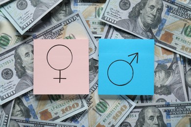 Photo of Gender pay gap. Paper notes with male and female symbols on dollar banknotes, flat lay