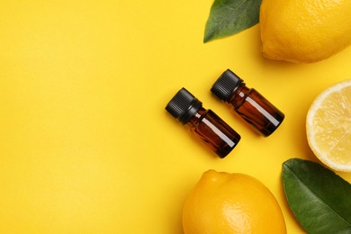Bottles of citrus essential oil, fresh lemons and leaves on yellow background, flat lay. Space for text
