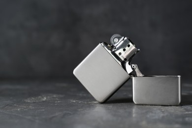Photo of Metallic cigarette lighter on gray textured table against dark background, closeup