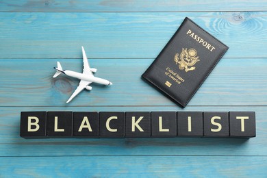 Black cubes with word Blacklist, toy airplane and passport on turquoise wooden background, flat lay