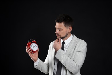 Businessman holding alarm clock on black background. Time management