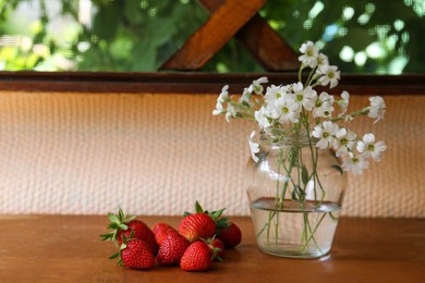Photo of Fresh strawberries and bouquet of beautiful white snow-in-summer flowers on wooden table. Space for text