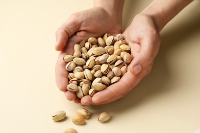 Photo of Woman holding tasty roasted pistachio nuts on beige background, closeup