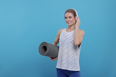 Photo of Sportswoman with headphones and fitness mat on light blue background, space for text