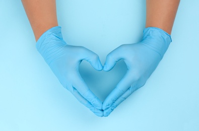 Person in latex gloves showing heart gesture against light blue background, closeup on hands