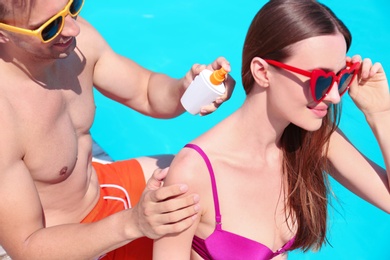Young man applying sun protection cream onto girlfriend at swimming pool