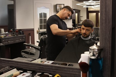 Professional hairdresser making stylish haircut near mirror in barbershop