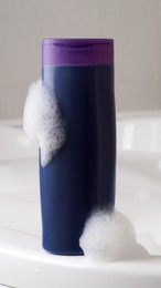 Purple bottle of bubble bath with foam on tub indoors