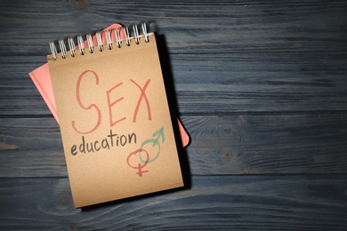 Notebook with phrase "SEX EDUCATION" and gender symbols on dark wooden background, top view. Space for text