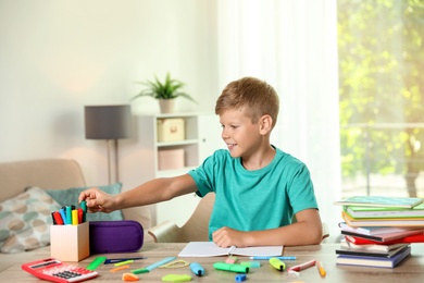 Photo of Cute boy doing homework at table with school stationery indoors