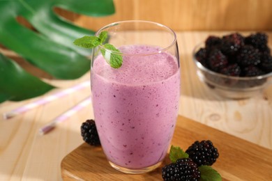 Delicious blackberry smoothie in glass and berries on wooden table, closeup