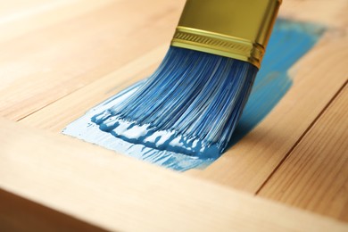 Applying blue paint onto wooden surface, closeup