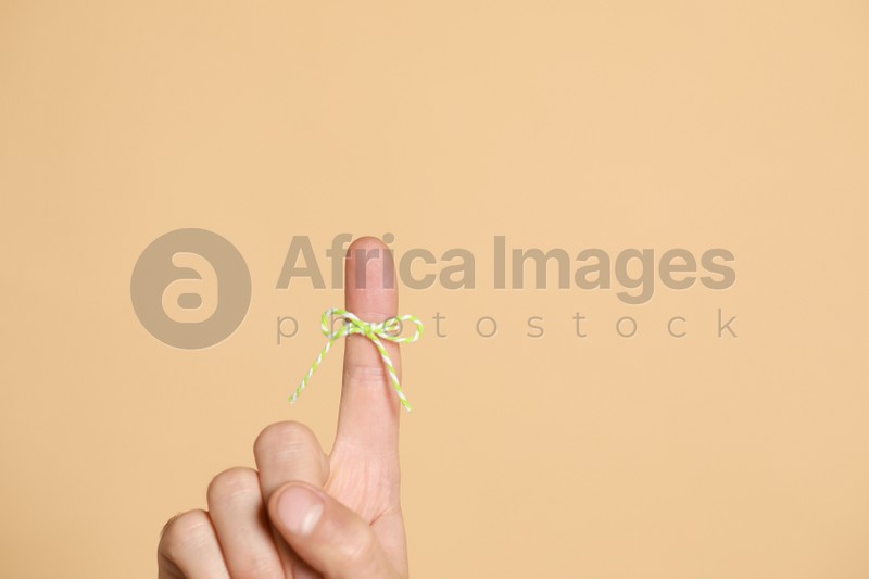 Man showing index finger with tied bow as reminder on beige background, closeup. Space for text