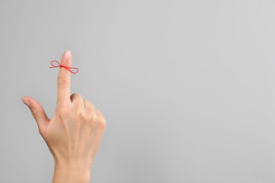 Woman showing index finger with tied red bow as reminder on light grey background, closeup. Space for text