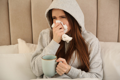 Sick young woman with cup of hot drink in bed at home. Influenza virus