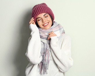 Young woman wearing warm sweater, scarf and hat on light background. Winter season