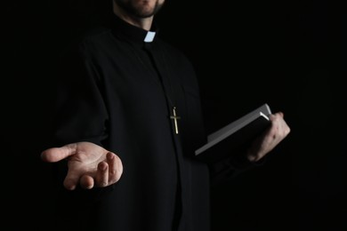 Priest with Bible praying on dark background, closeup