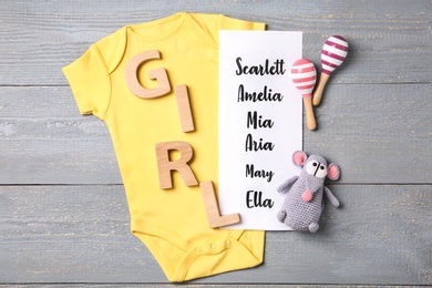 Bodysuit, list of baby names and toys on grey wooden background, flat lay