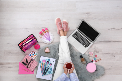 Beauty blogger with laptop and cosmetics sitting on floor, top view