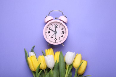 Photo of Pink alarm clock and beautiful tulips on violet background, flat lay. Spring time
