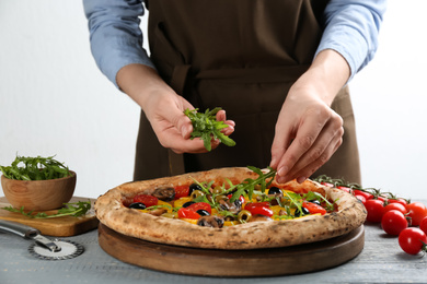 Woman adding arugula to vegetable pizza at table, closeup