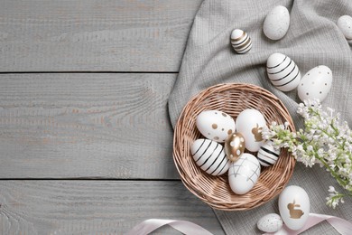 Photo of Many painted Easter eggs, branch with lilac flowers and ribbon on grey wooden table, flat lay. Space for text