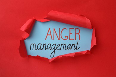 Words Anger Management on light blue background, view through hole in torn red paper