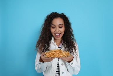 Excited African American woman with French fries on light blue background