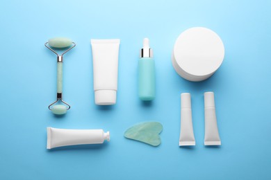 Natural face roller, gua sha tool and cosmetic products on light blue background, flat lay