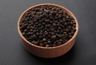 Wooden bowl of black peppercorns on dark background