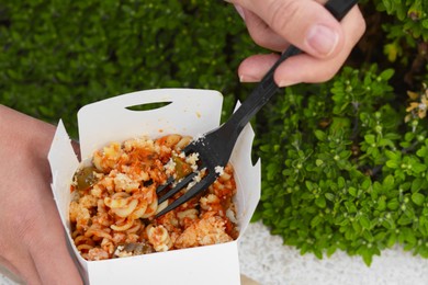 Woman eating takeaway noodles from paper box with fork outdoors, closeup. Street food